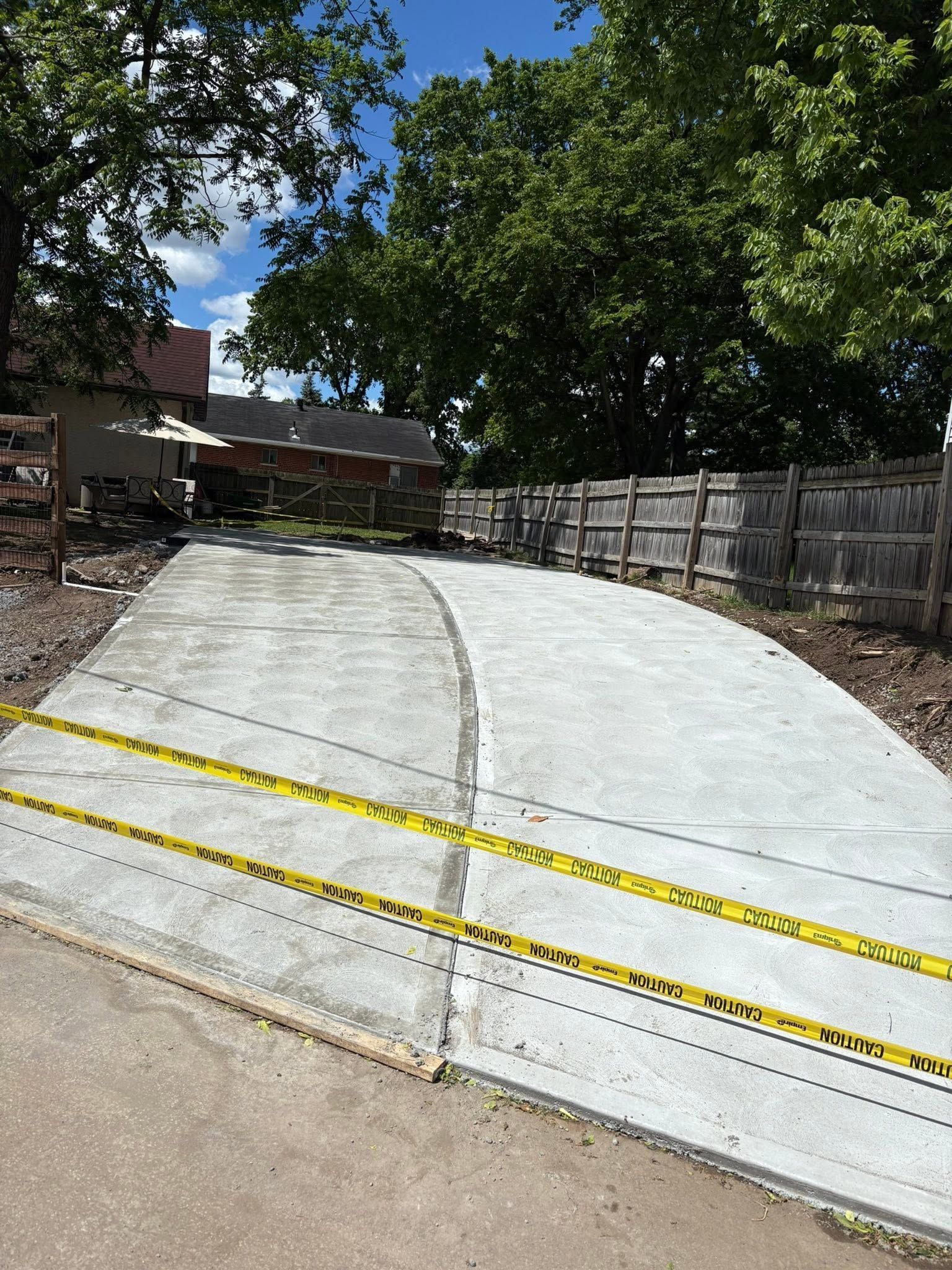 Concrete driveway ramp with yellow caution stripes beside a wooden fence and trees