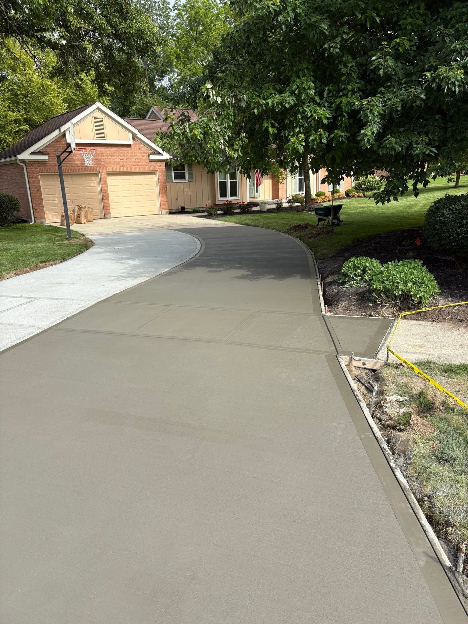 Fresh concrete driveway curving toward a brick house with trees and shrubs along the side