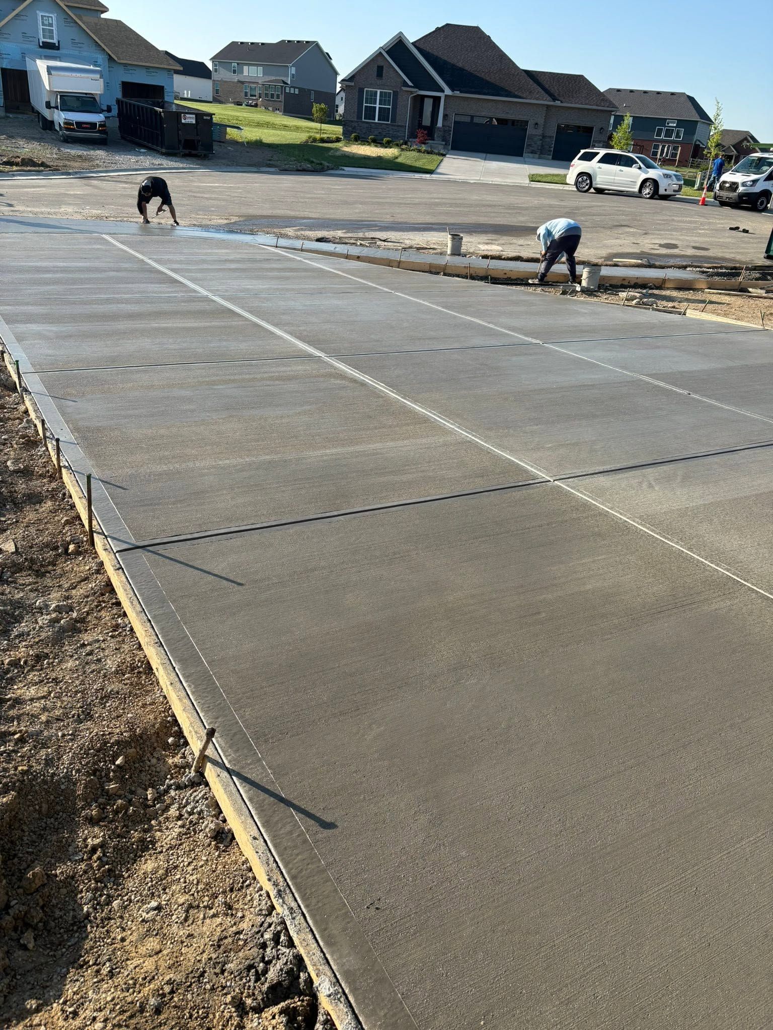 Workers smoothing a concrete driveway slab at a suburban housing site