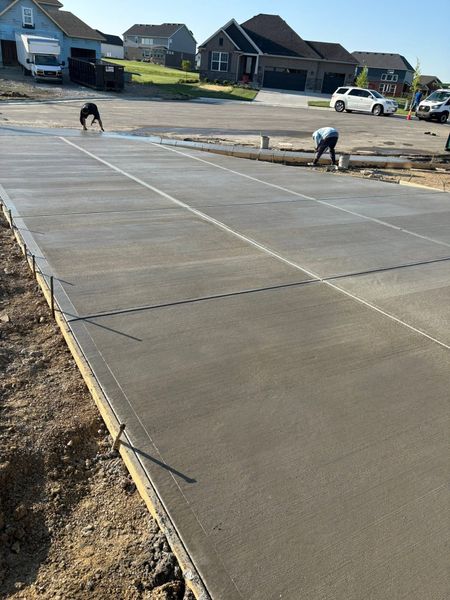 Workers smoothing a concrete driveway slab at a suburban housing site
