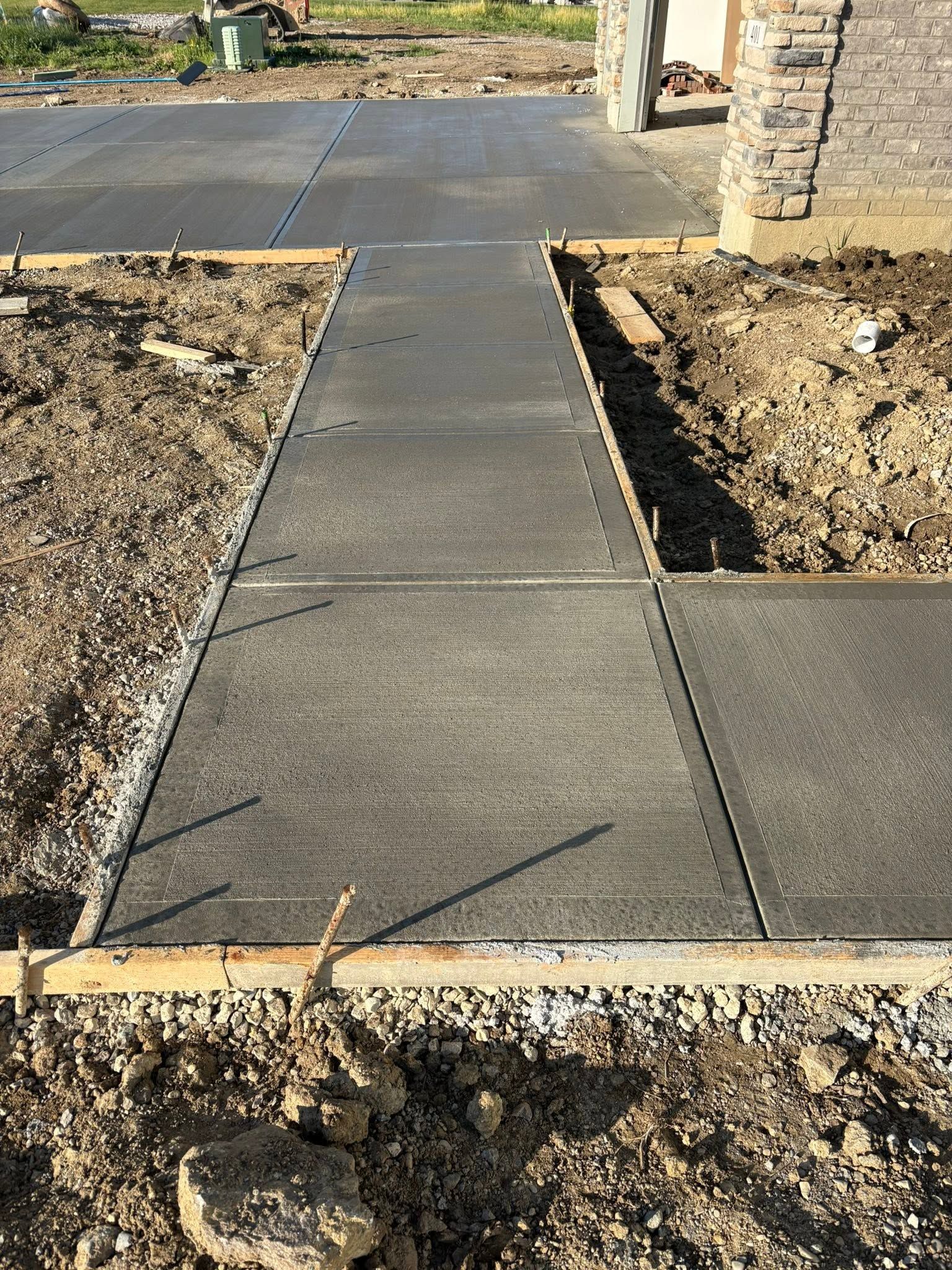 Concrete walkway leading to a house entrance, bordered by bare dirt and fresh construction work.