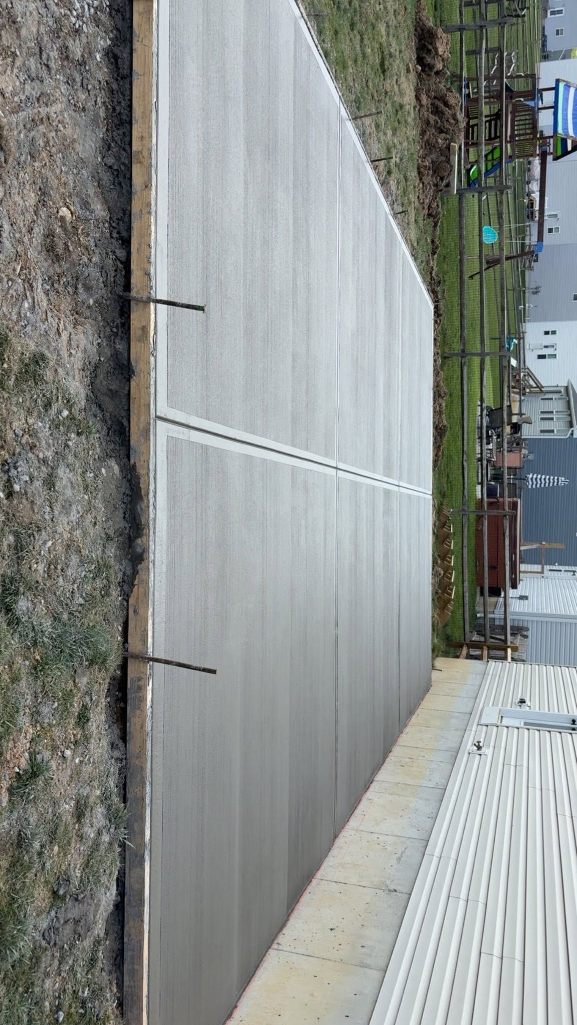 Concrete patio next to a white-sided building, with gravel, steps, and a grassy yard beyond.