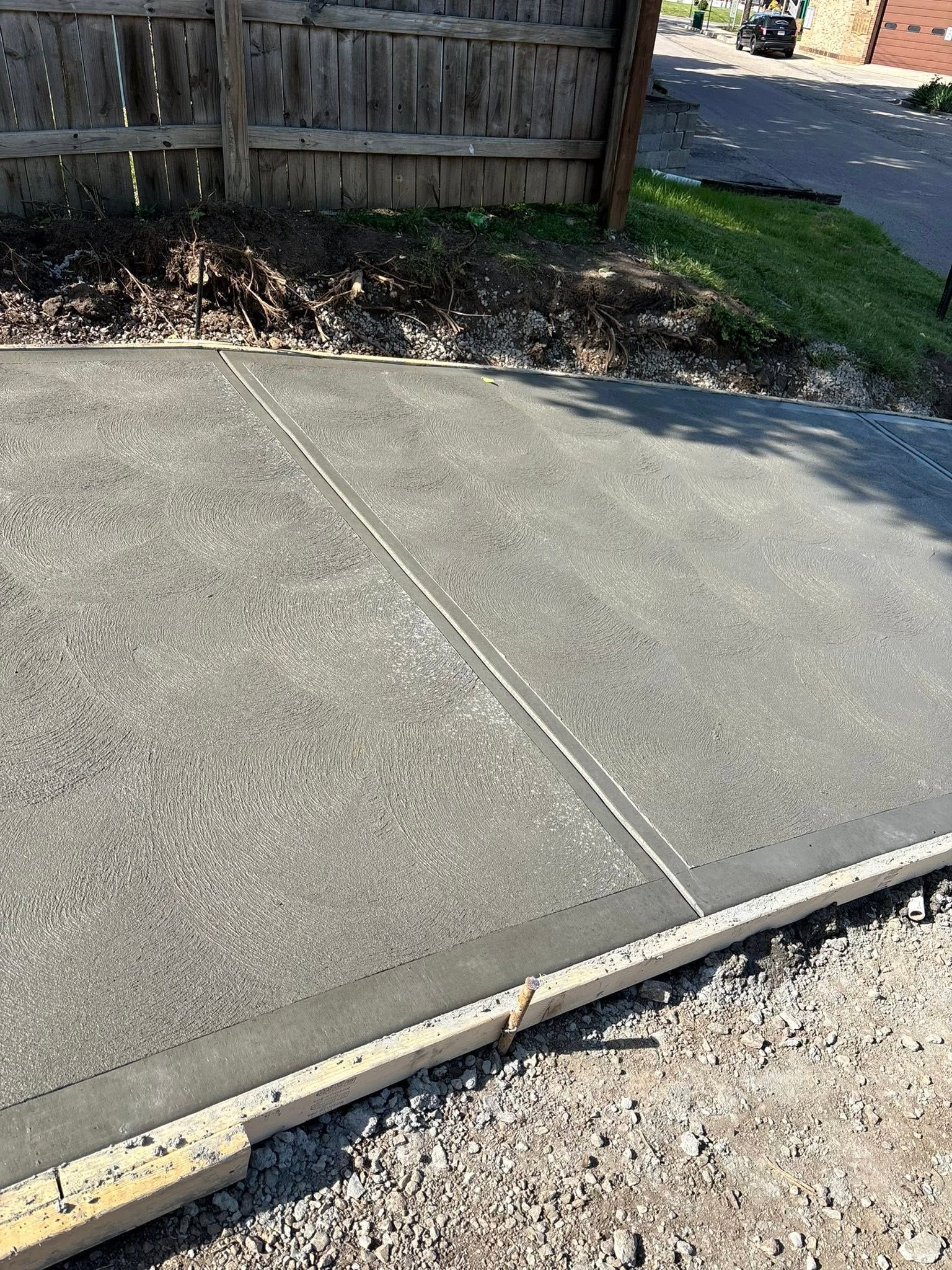 Cracked concrete driveway beside a wooden fence and gravel edge