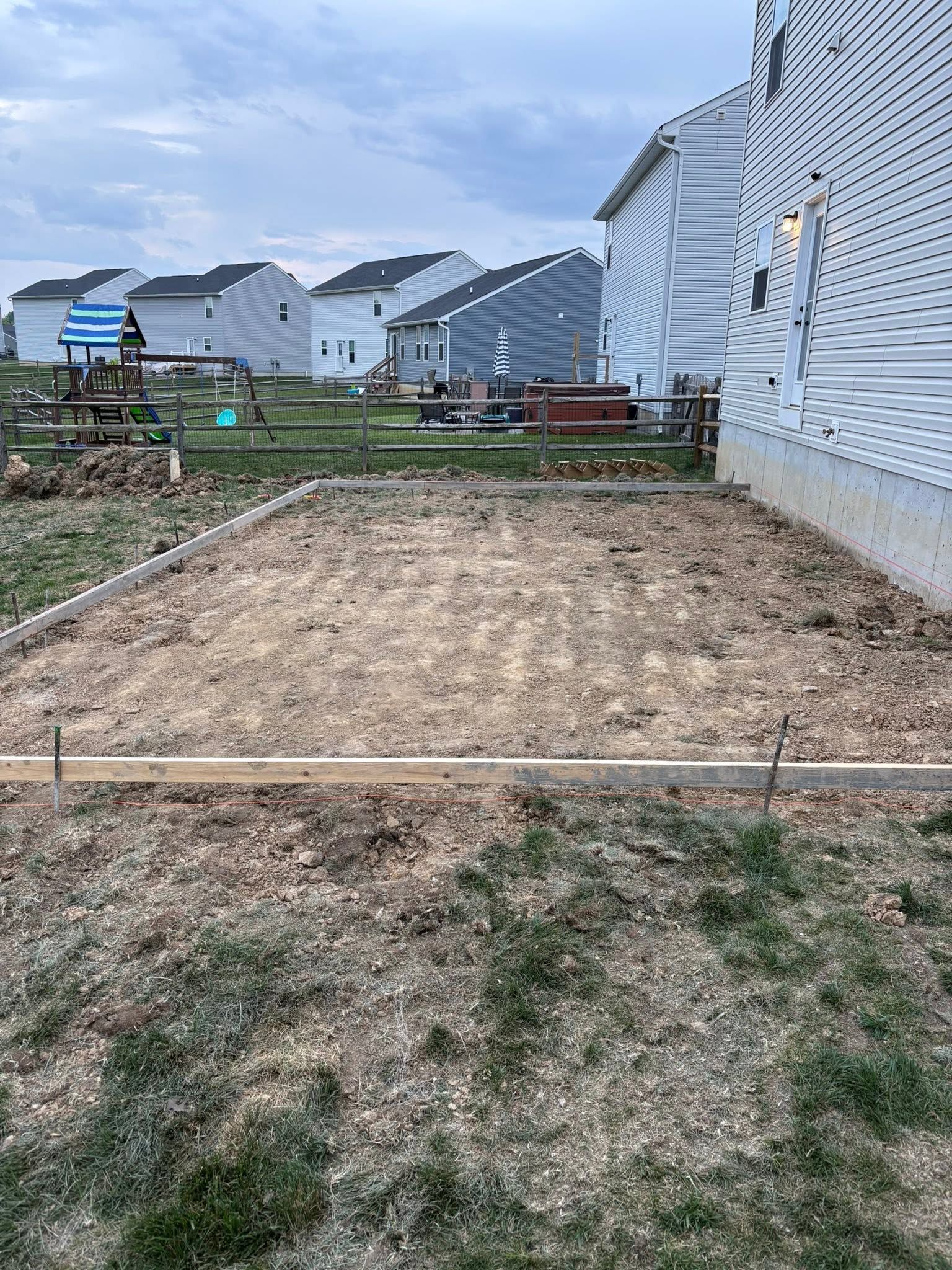 Empty dirt lot beside white houses and a striped building under a cloudy sky.