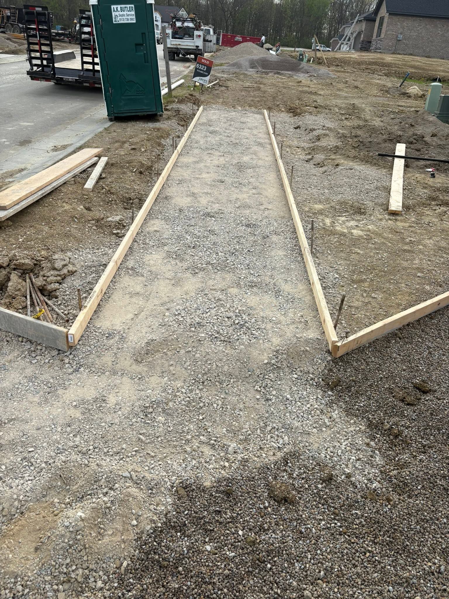Gravel walkway under construction with wooden edging and a portable toilet nearby