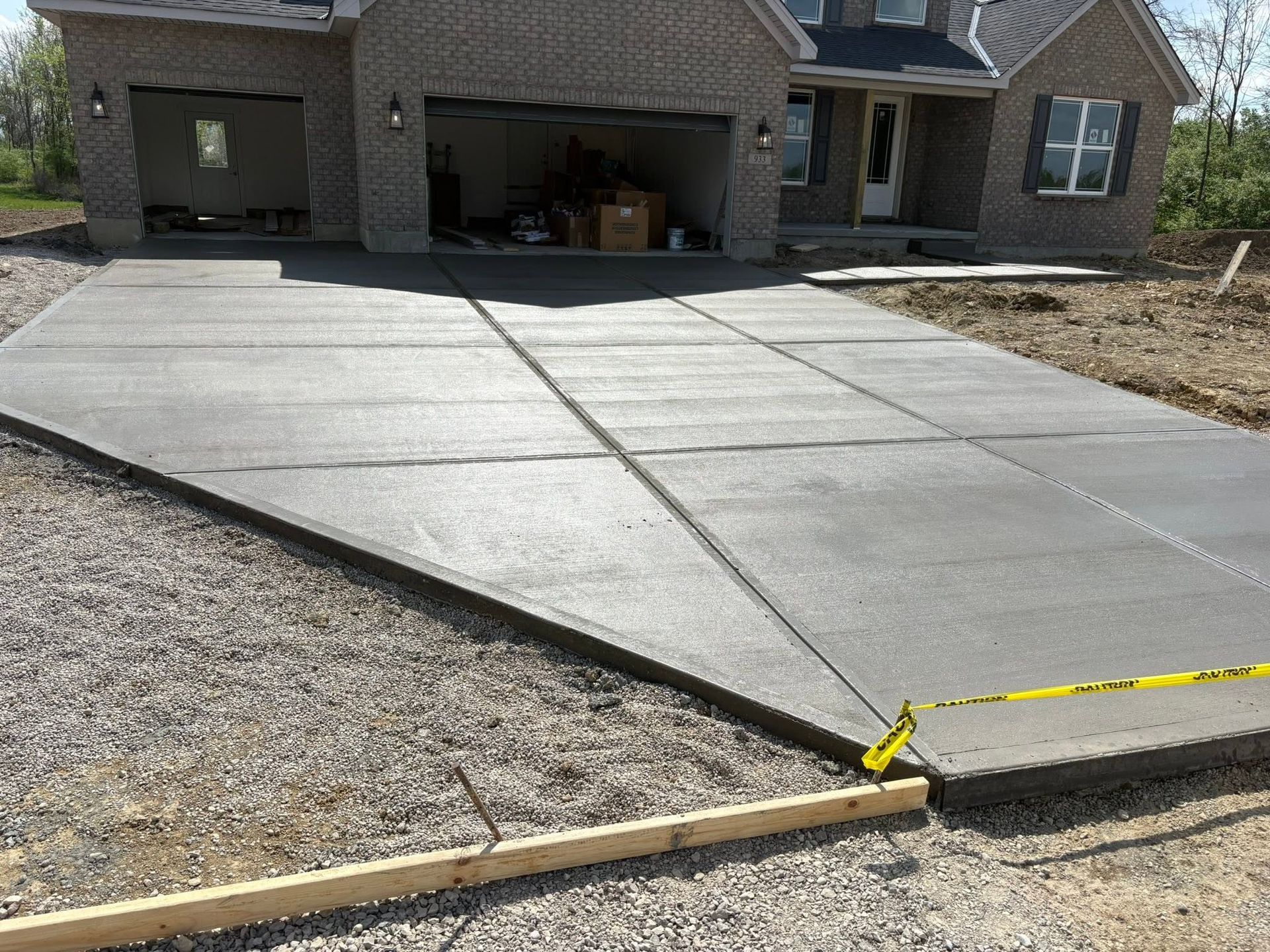 Concrete driveway beside a brick house, with a yellow caution tape blocking the edge.