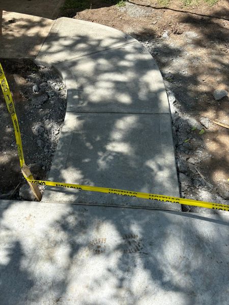 Concrete sidewalk repair area marked with yellow caution tape in a shaded outdoor scene