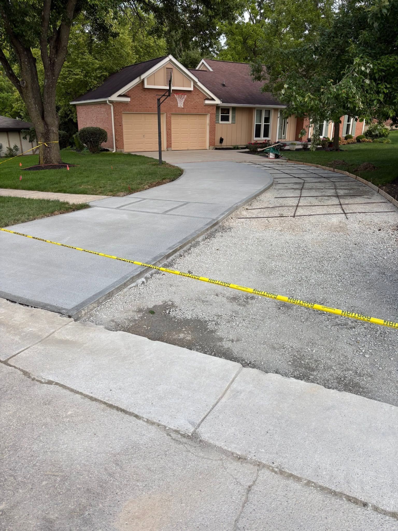 Cracked residential driveway with yellow caution tape in front of a brick house and lawn