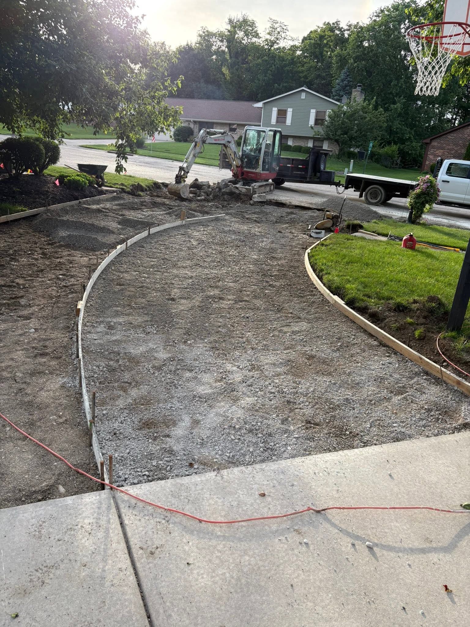 Curved gravel pathway under construction beside a street, with a small tractor and landscaping materials nearby.