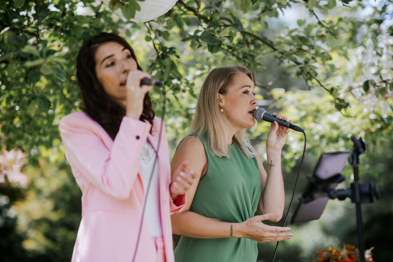 Zangduo Remedy treedt buiten op, de ene in een roze jasje en de andere in een groene jurk, beiden zingend in een microfoon. Bruiloft. 