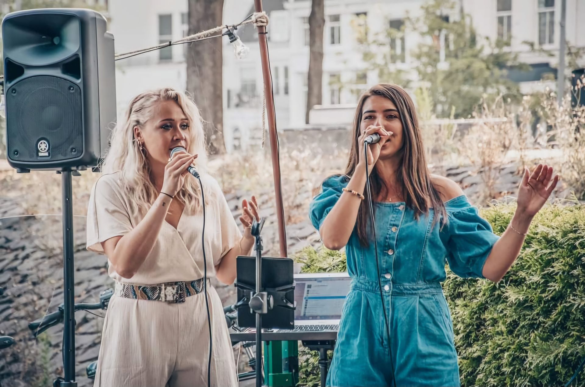 Twee zangers treden buiten op met microfoons en een luidspreker tijdens een straatevenement.