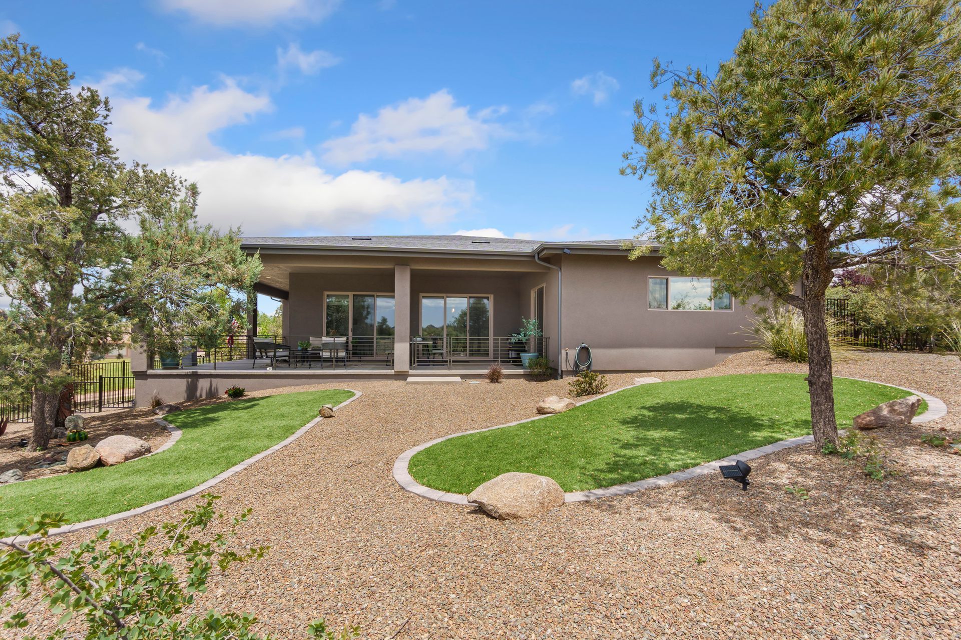 Modern single-story house with a covered patio, landscaped yard, and gravel driveway under a blue sky