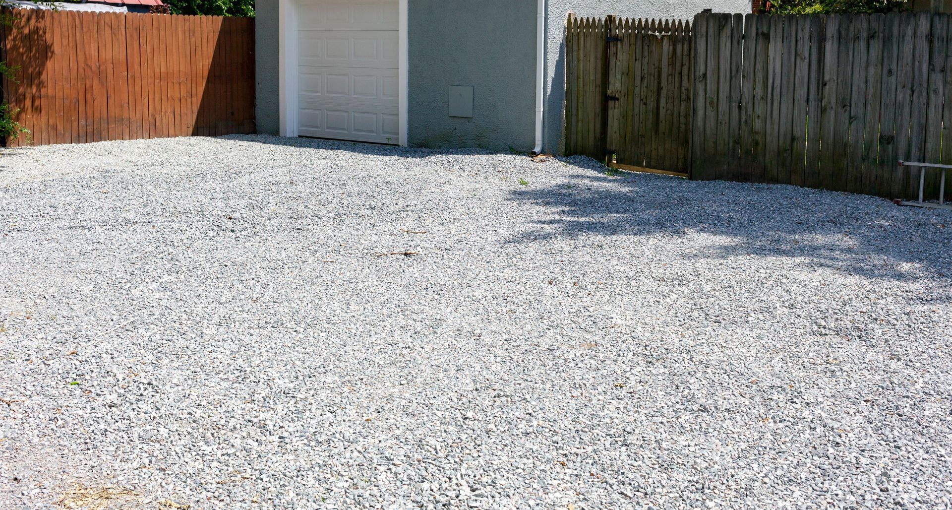 Gravel-covered driveway beside a white garage, bordered by wooden fences on both sides.
