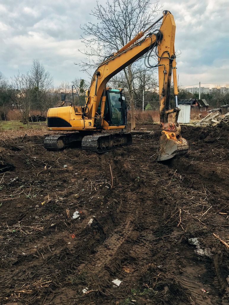 Yellow excavator clearing muddy ground under a cloudy sky