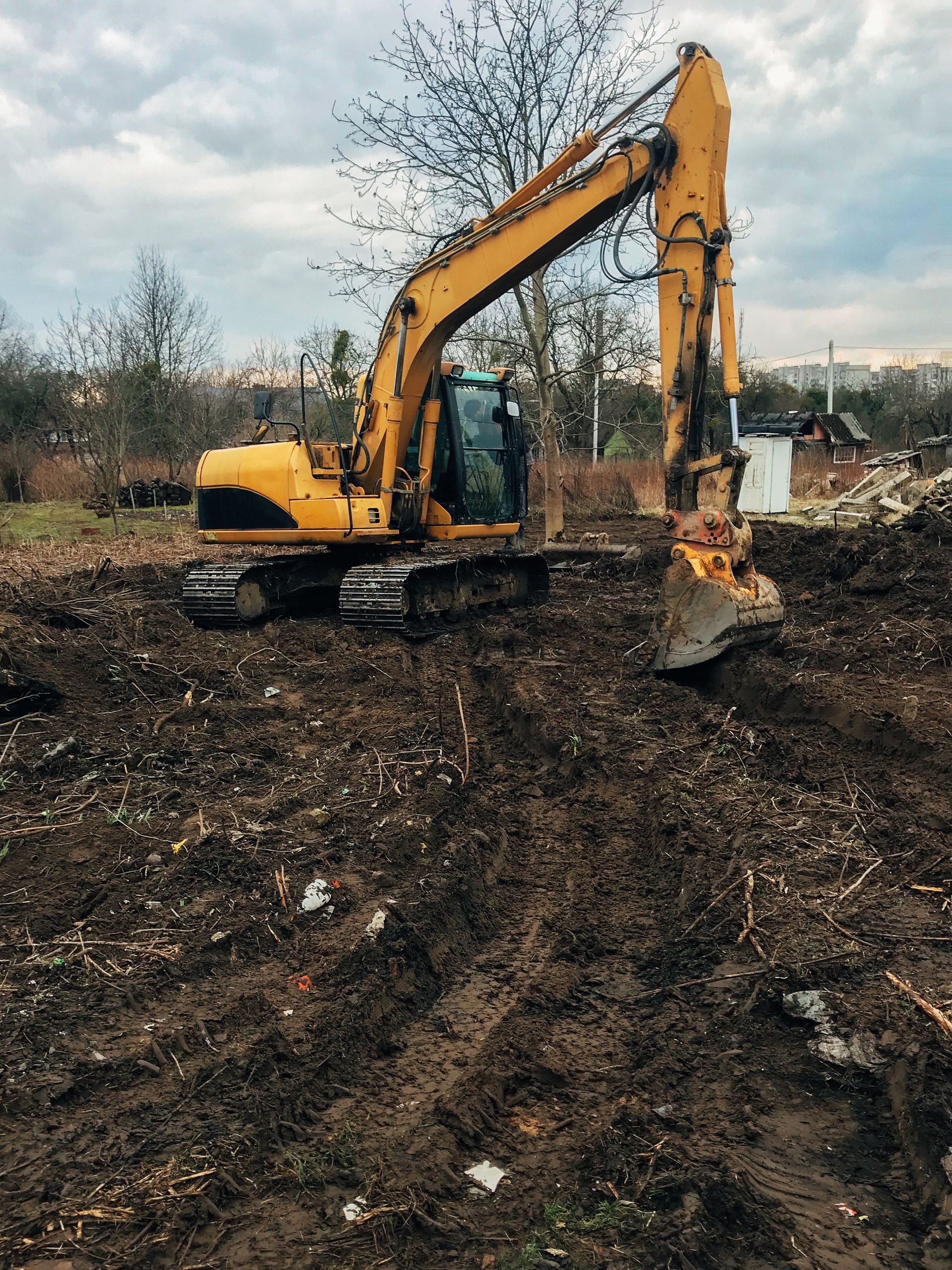 Yellow excavator clearing muddy ground under a cloudy sky