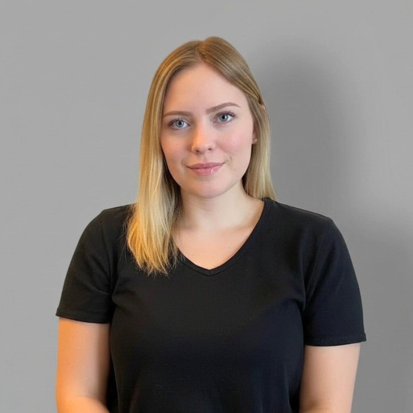 Woman in a black V-neck shirt against a plain gray background, facing the camera with a slight smile
