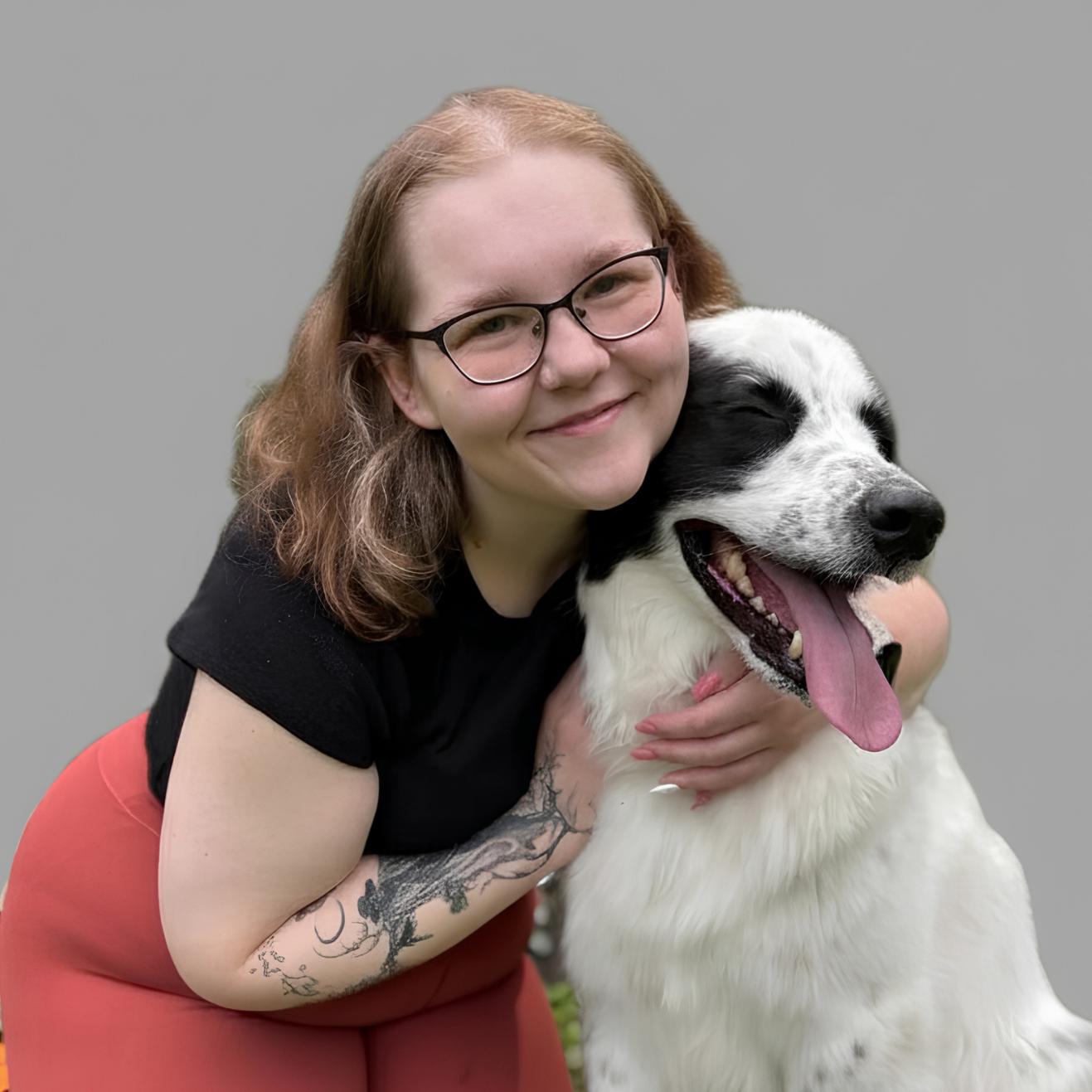 Woman with glasses hugging a black-and-white dog against a gray background
