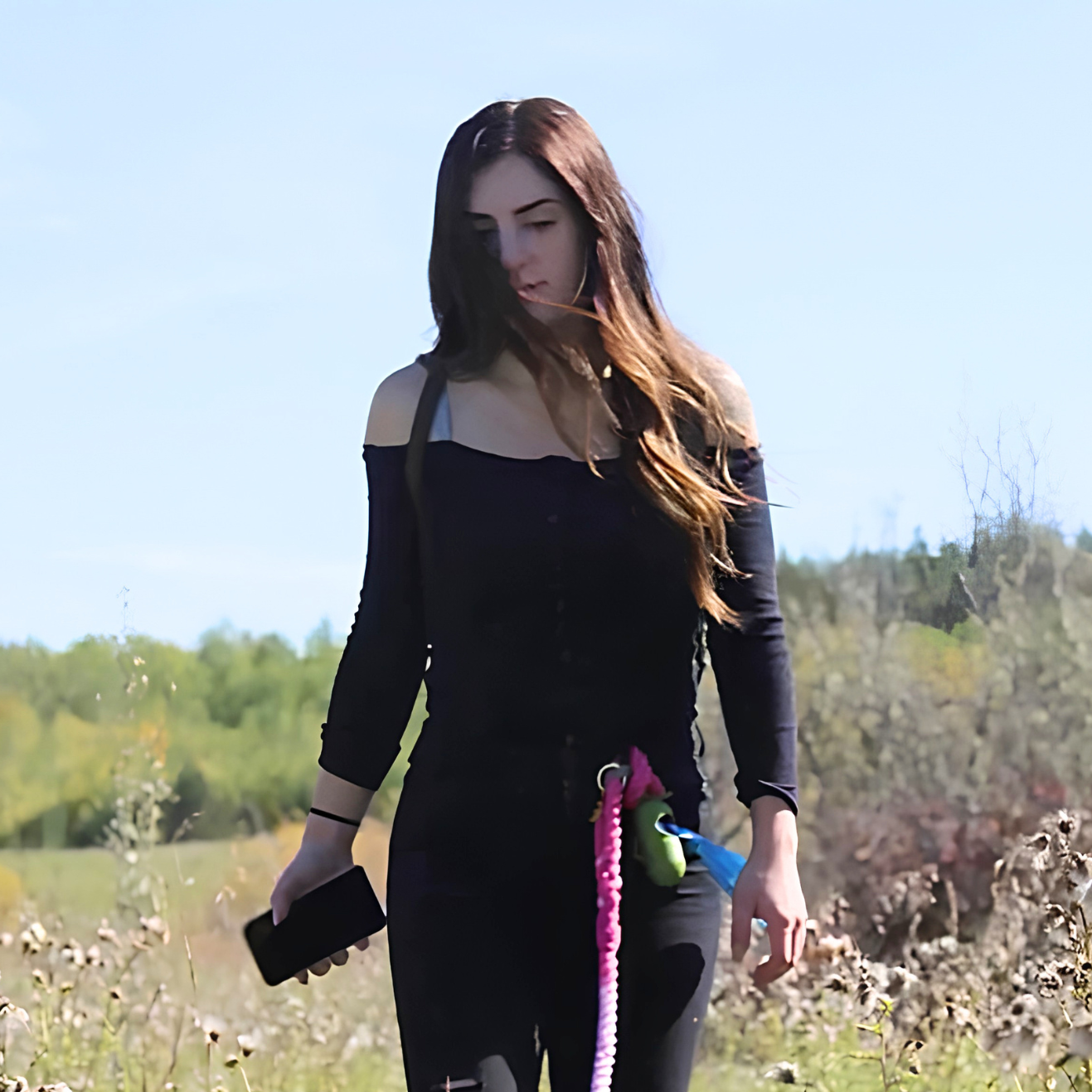 Woman in black top holding a phone and colorful rope in a sunny field