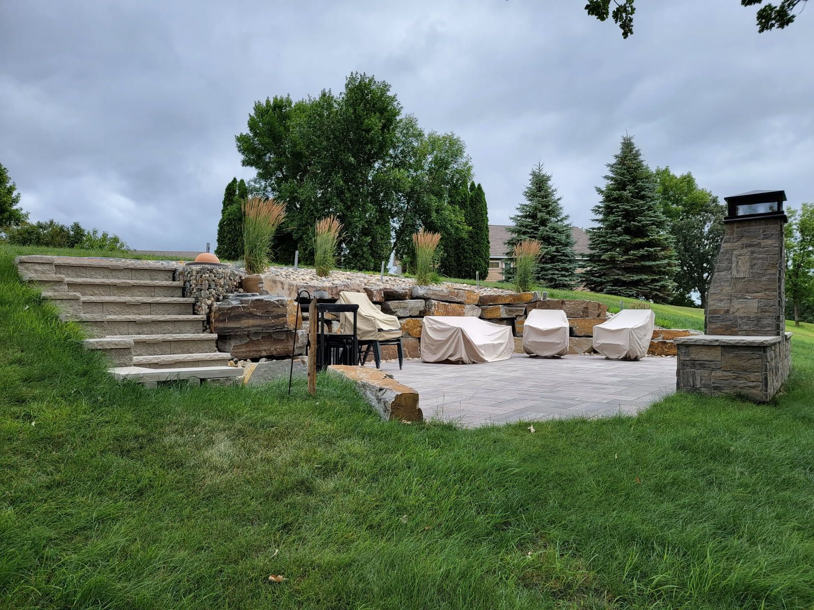 A patio with a fire pit , stairs , chairs and a fireplace.