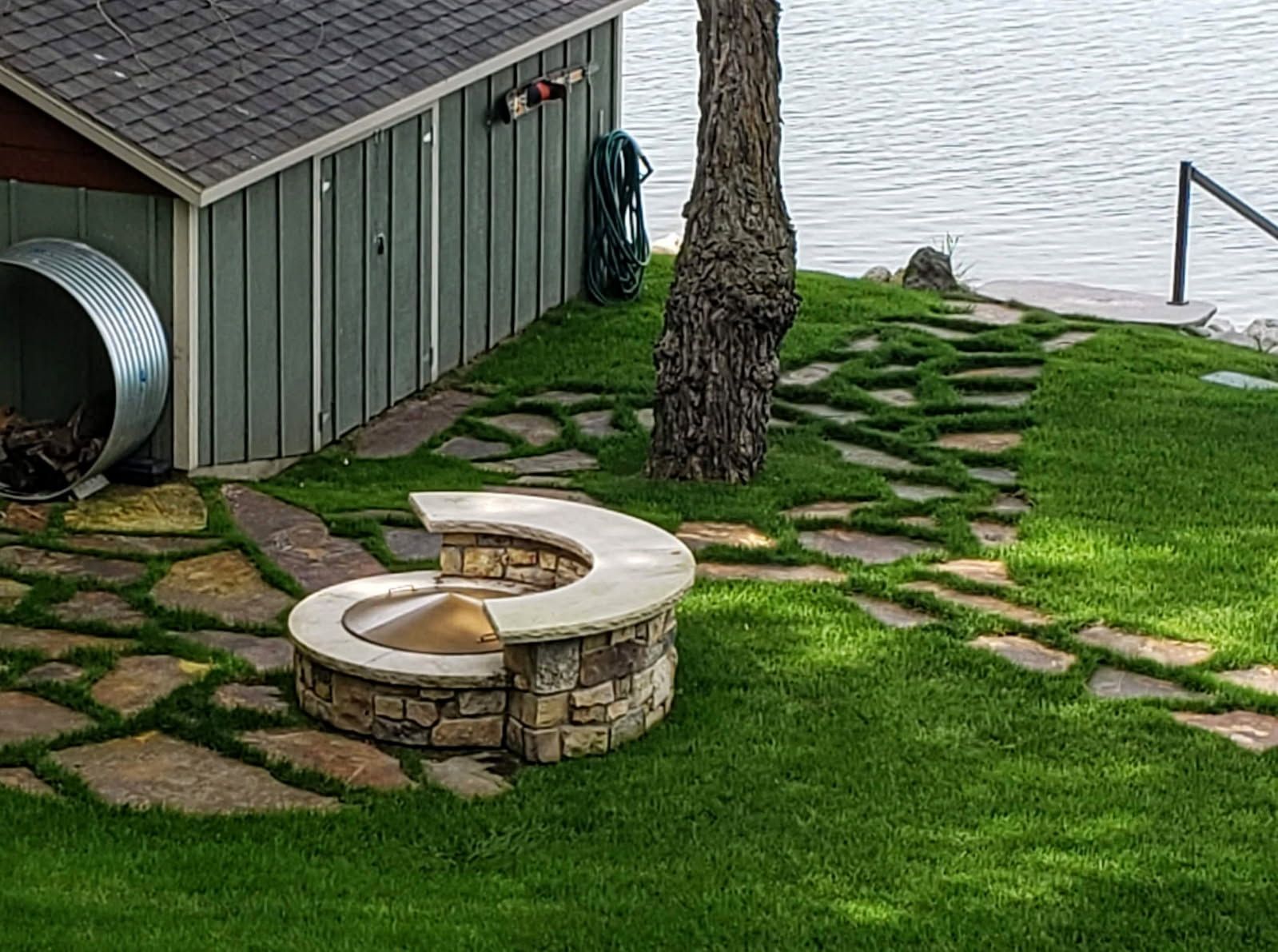 A fire pit is sitting in the middle of a lush green lawn next to a shed.