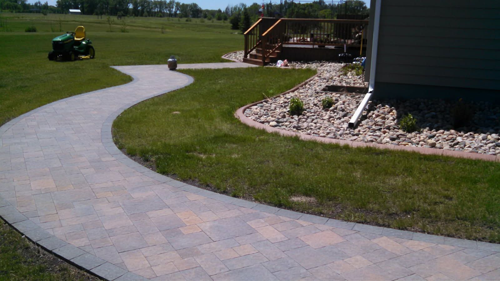 A walkway leading to a house with a lawn mower in the background.