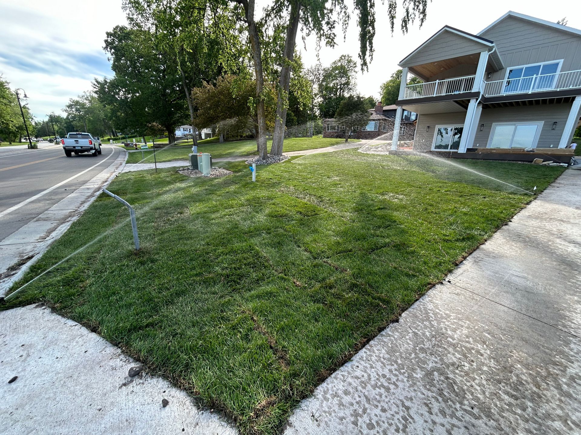 A lawn with a sprinkler on it and a house in the background.