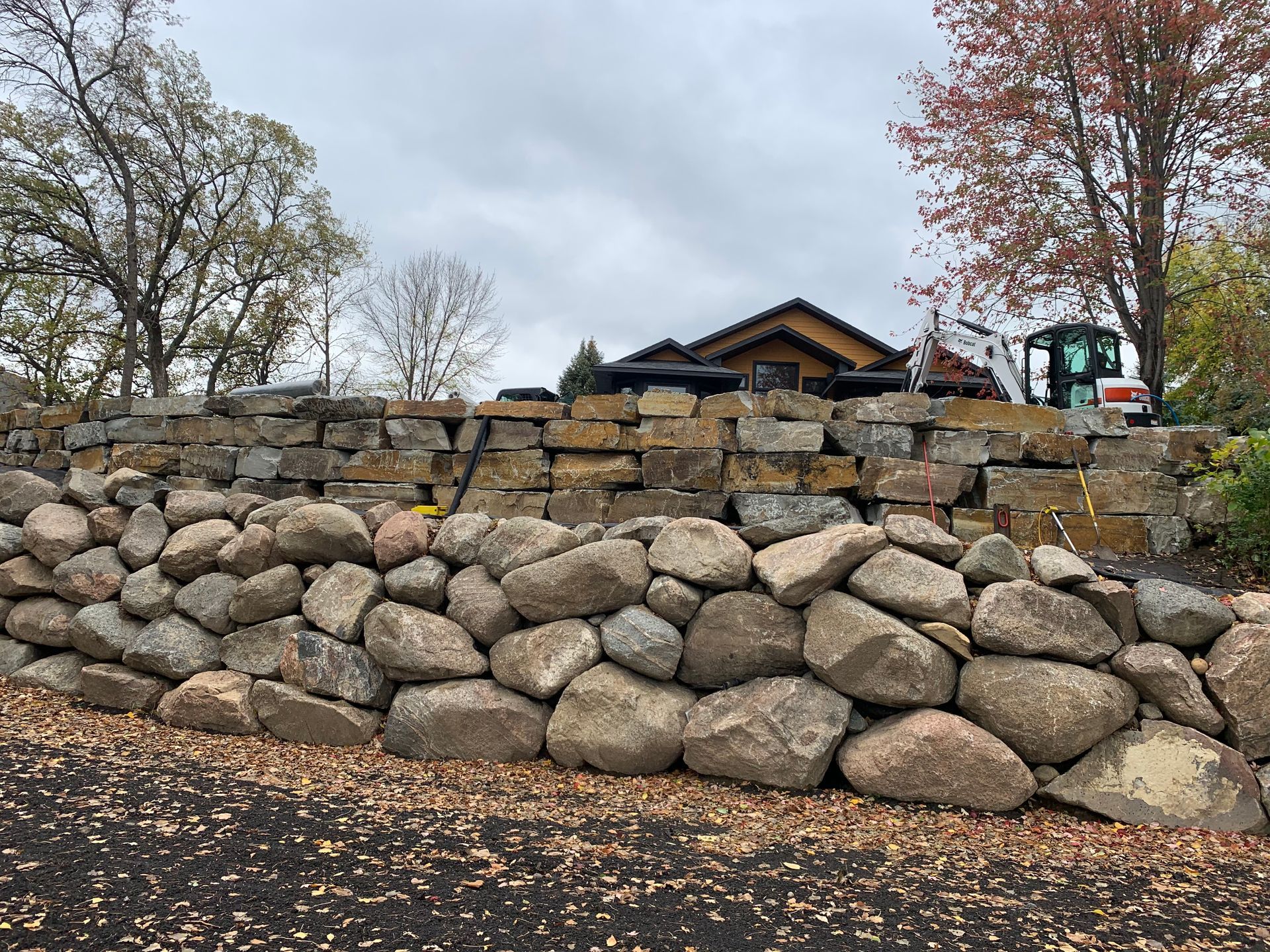 A large rock wall with a house in the background.