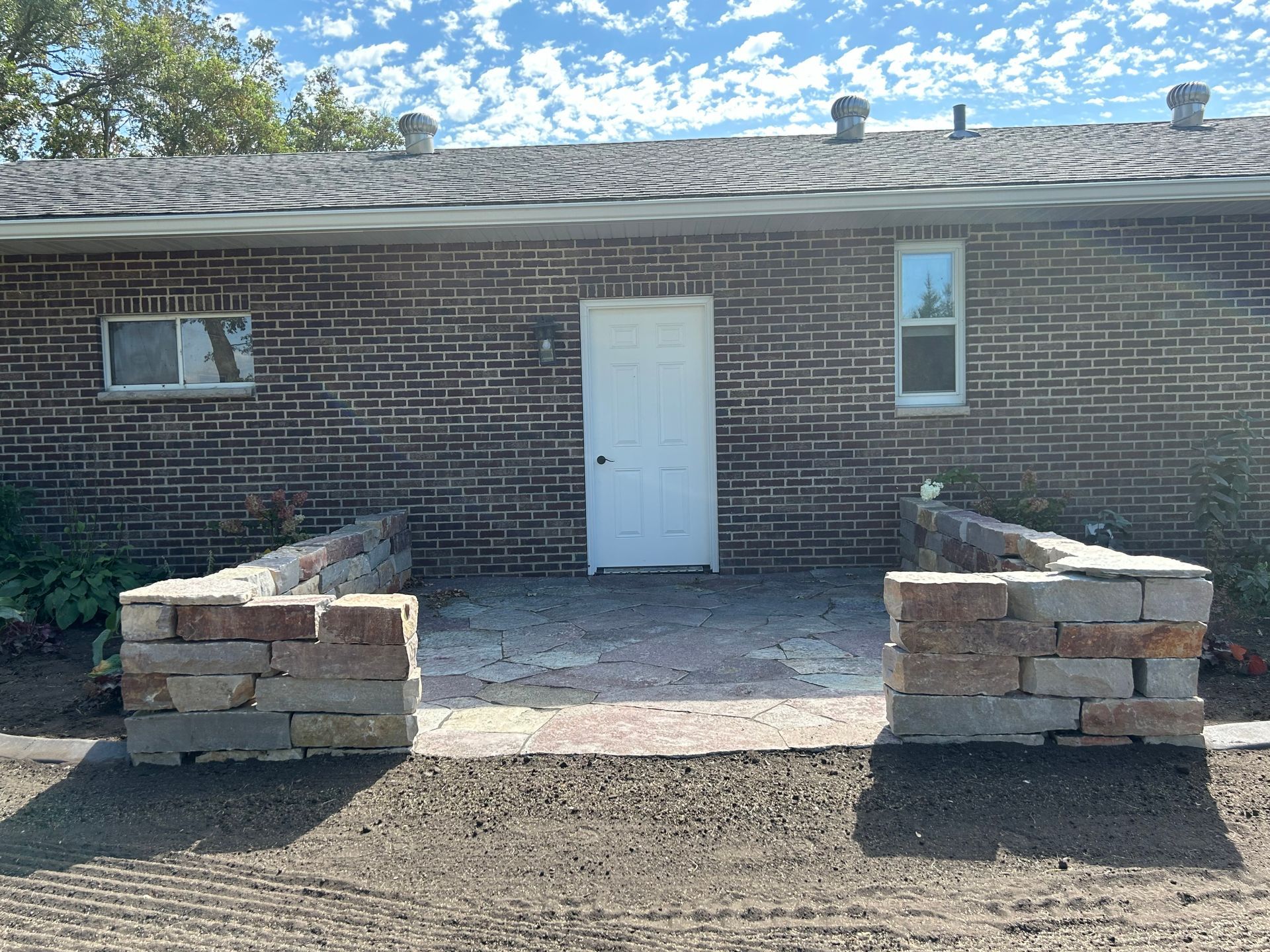 A brick house with a white door and a patio in front of it.