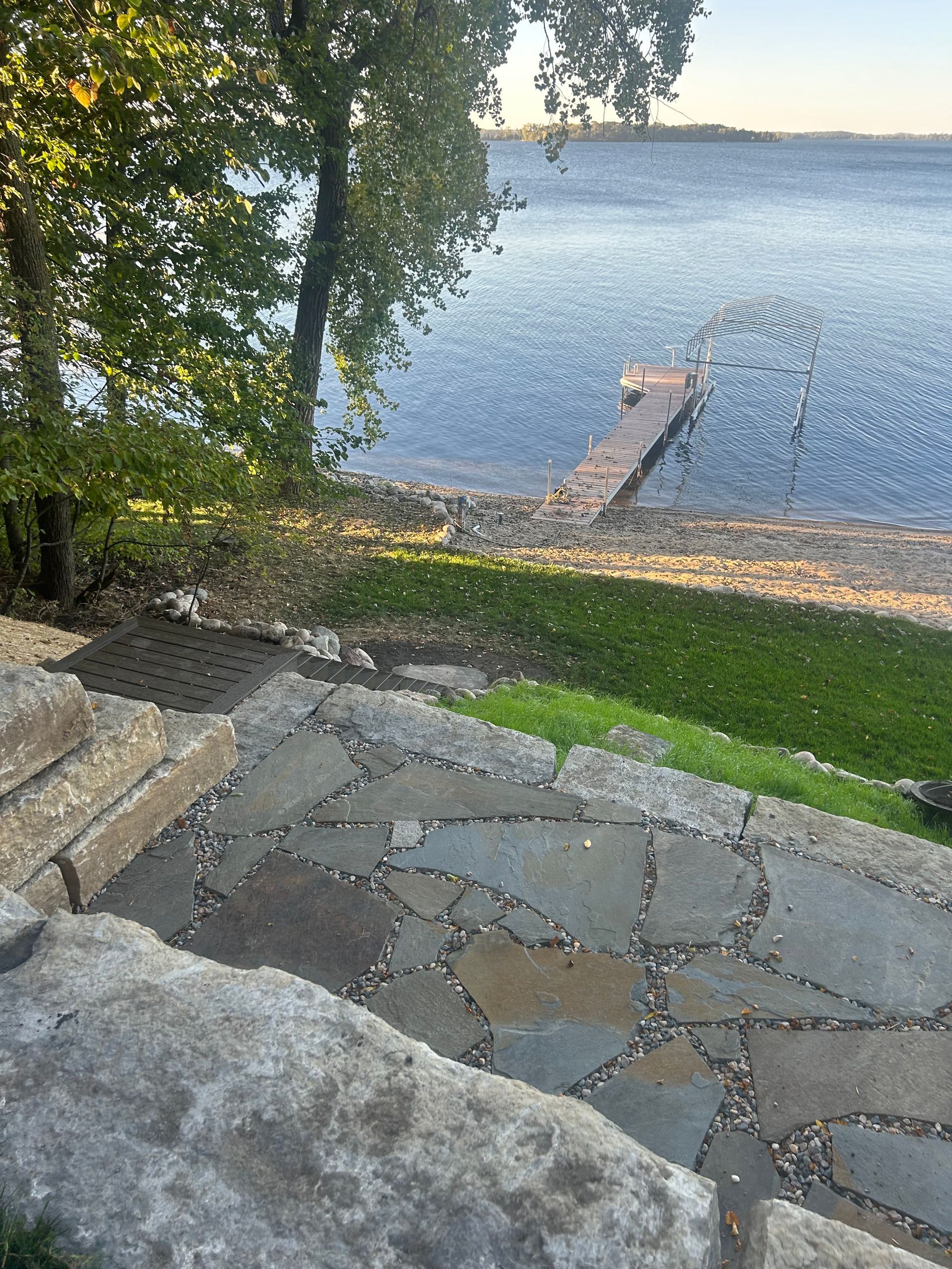 A stone walkway leading to a lake with a dock in the background.