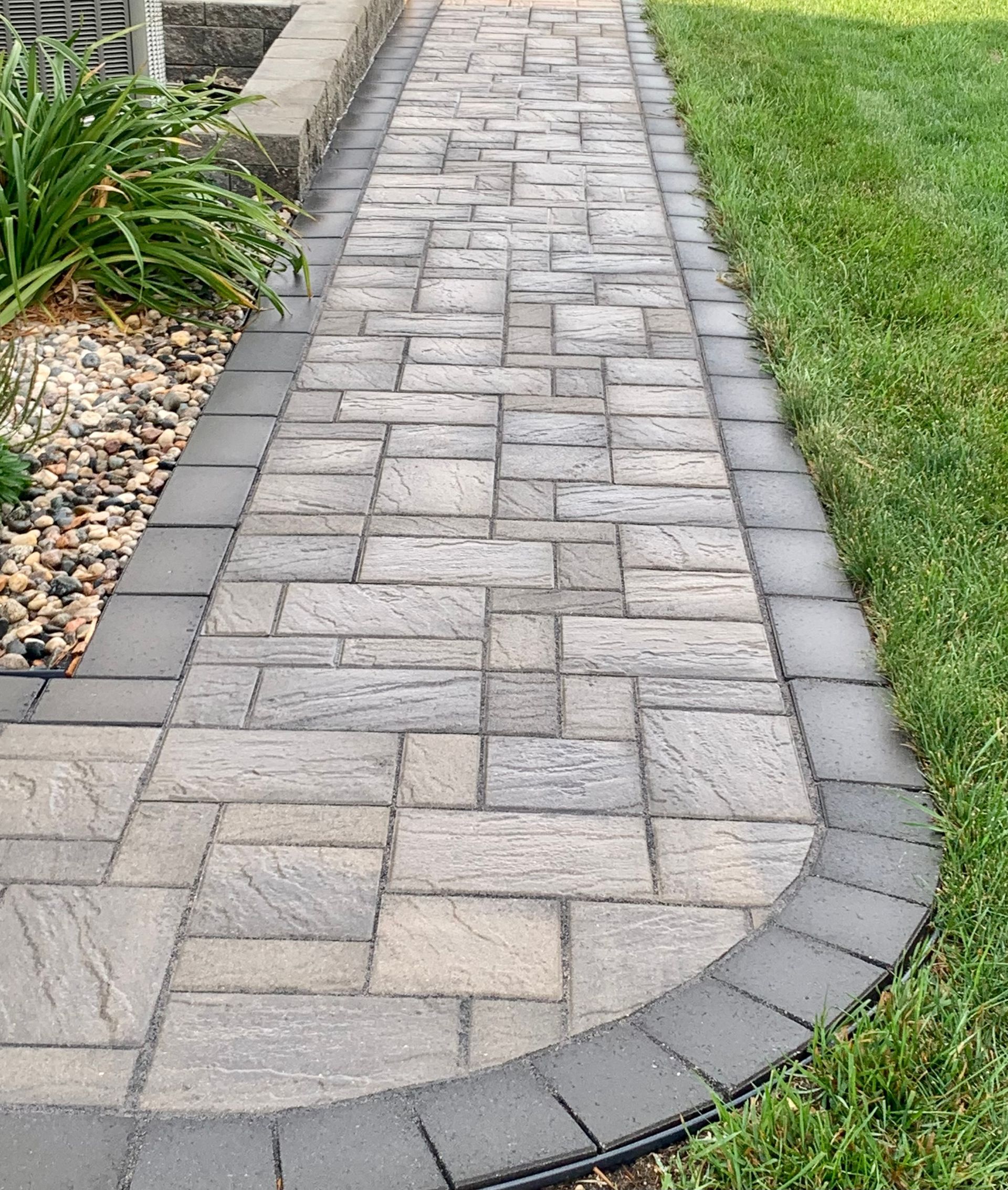 A brick walkway going through a lush green yard.
