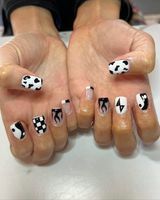 A close up of a person 's hands with black and white cow print nails.