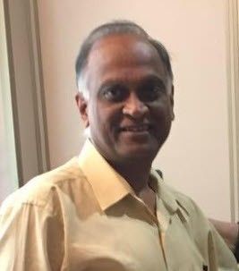 A man in a tan shirt is smiling for the camera.