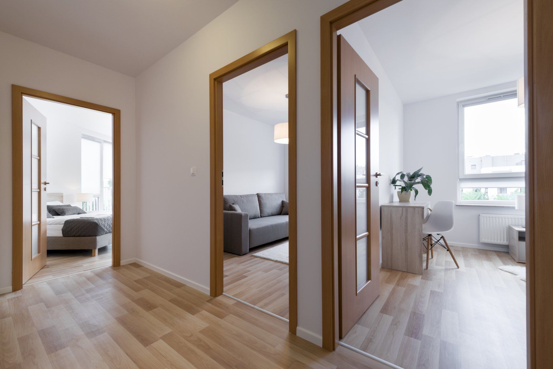Couloir lumineux avec portes ouvertes donnant sur une chambre, un salon et une pièce ensoleillée pouvant servir de bureau.