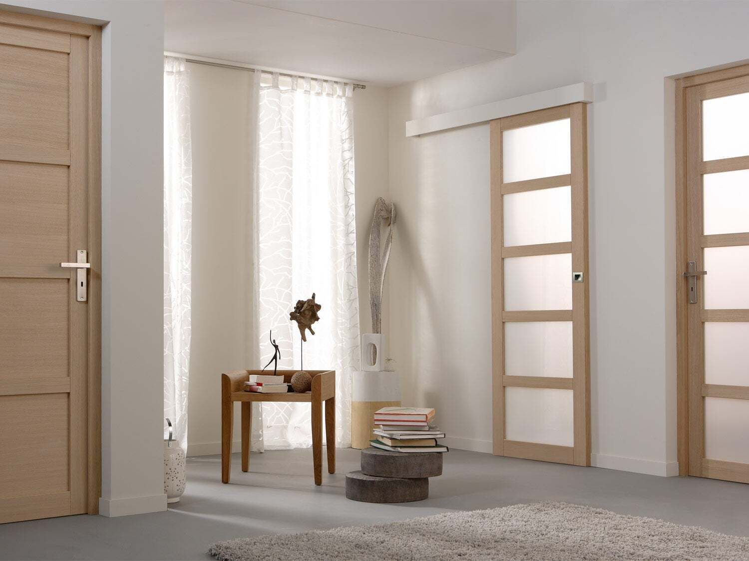 Couloir lumineux avec portes ouvertes donnant sur une chambre, un salon et une pièce ensoleillée pouvant servir de bureau.