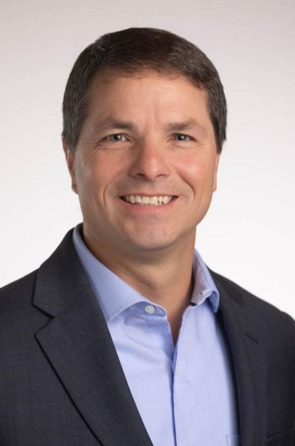 A man in a suit and blue shirt is smiling for the camera.