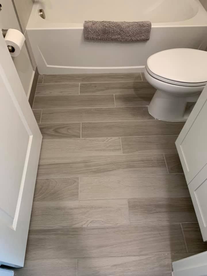 Small bathroom with gray tile floor, white toilet, bathtub, and a gray towel on the tub ledge.