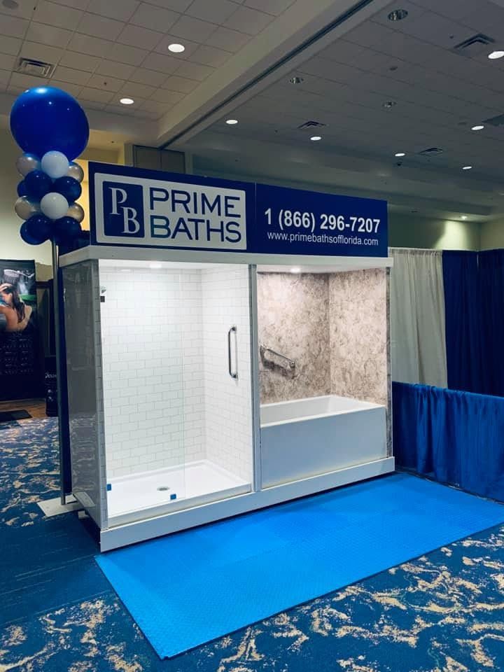 Prime Baths trade show booth with blue-and-white shower display and balloon column on a blue carpeted floor