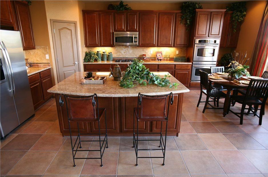 Modern kitchen with wood cabinets, large island, bar stools, and dining table near built-in ovens