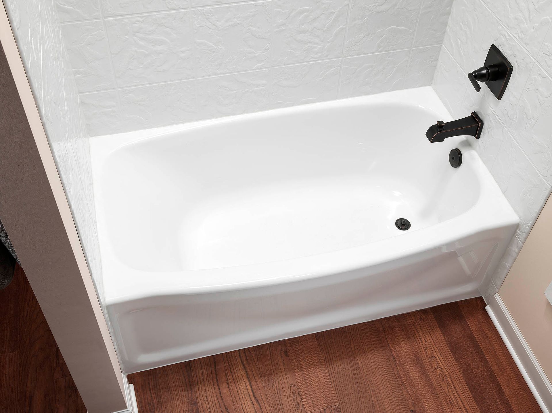 Small white bathtub with wall-mounted faucet in a bathroom with wood-look floor and light walls