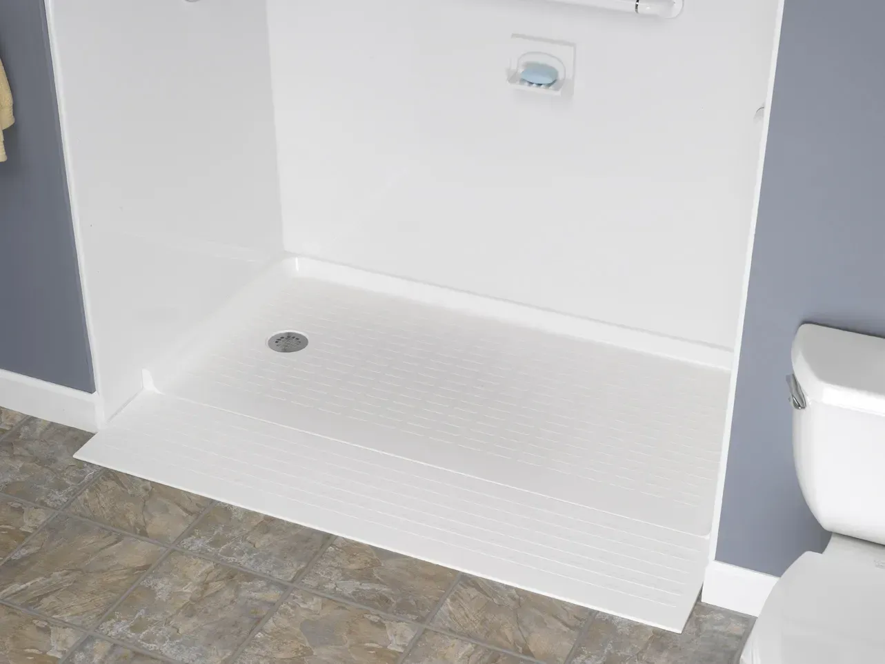 White accessible shower stall with built-in bench and grab bars beside a toilet in a bathroom.