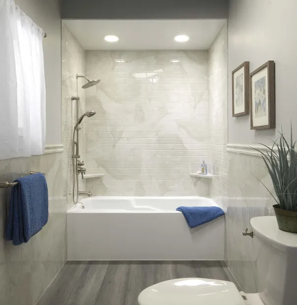 Bright bathroom with white tub, gray floor, blue towels, shower, and two framed pictures.