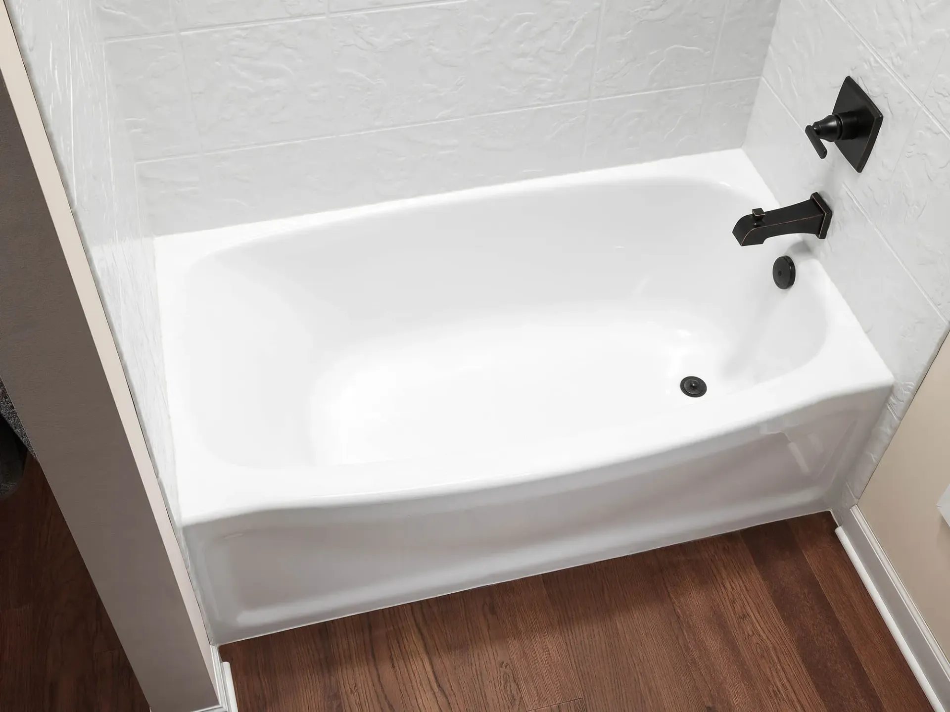 Small white bathtub with black fixtures in a bathroom with wood-look flooring