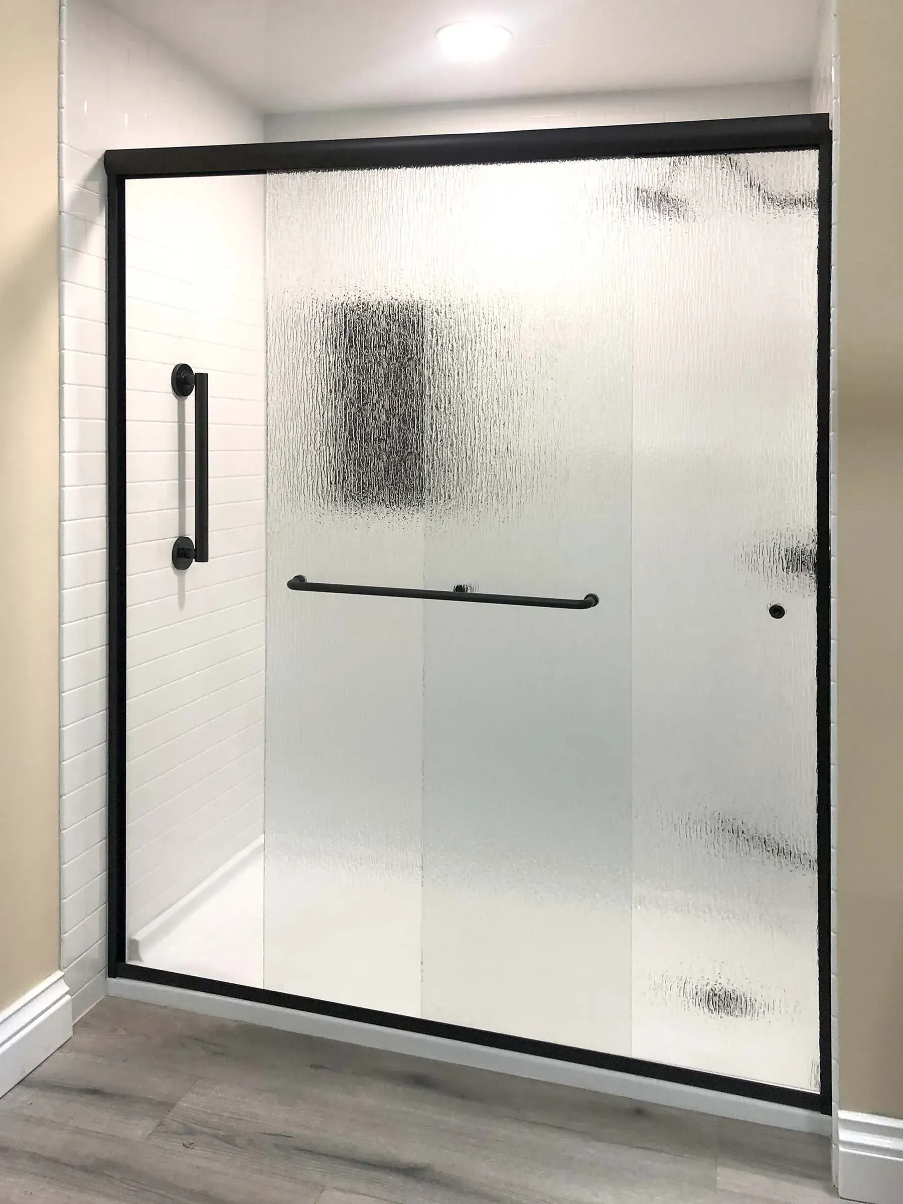 Frosted glass shower door with black frame and handle in a bathroom.