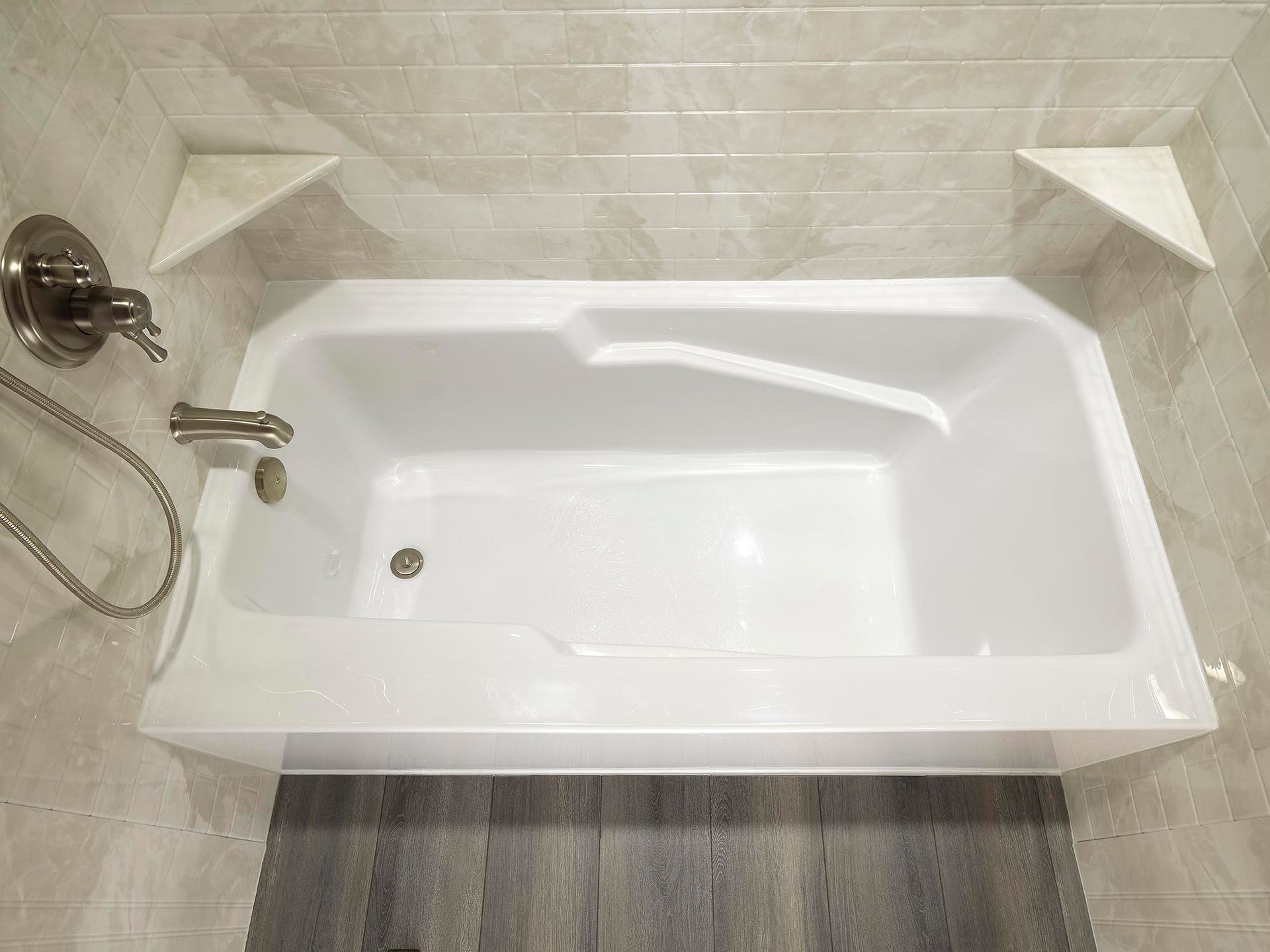 Clean white bathtub with beige tile surround and chrome shower fixtures