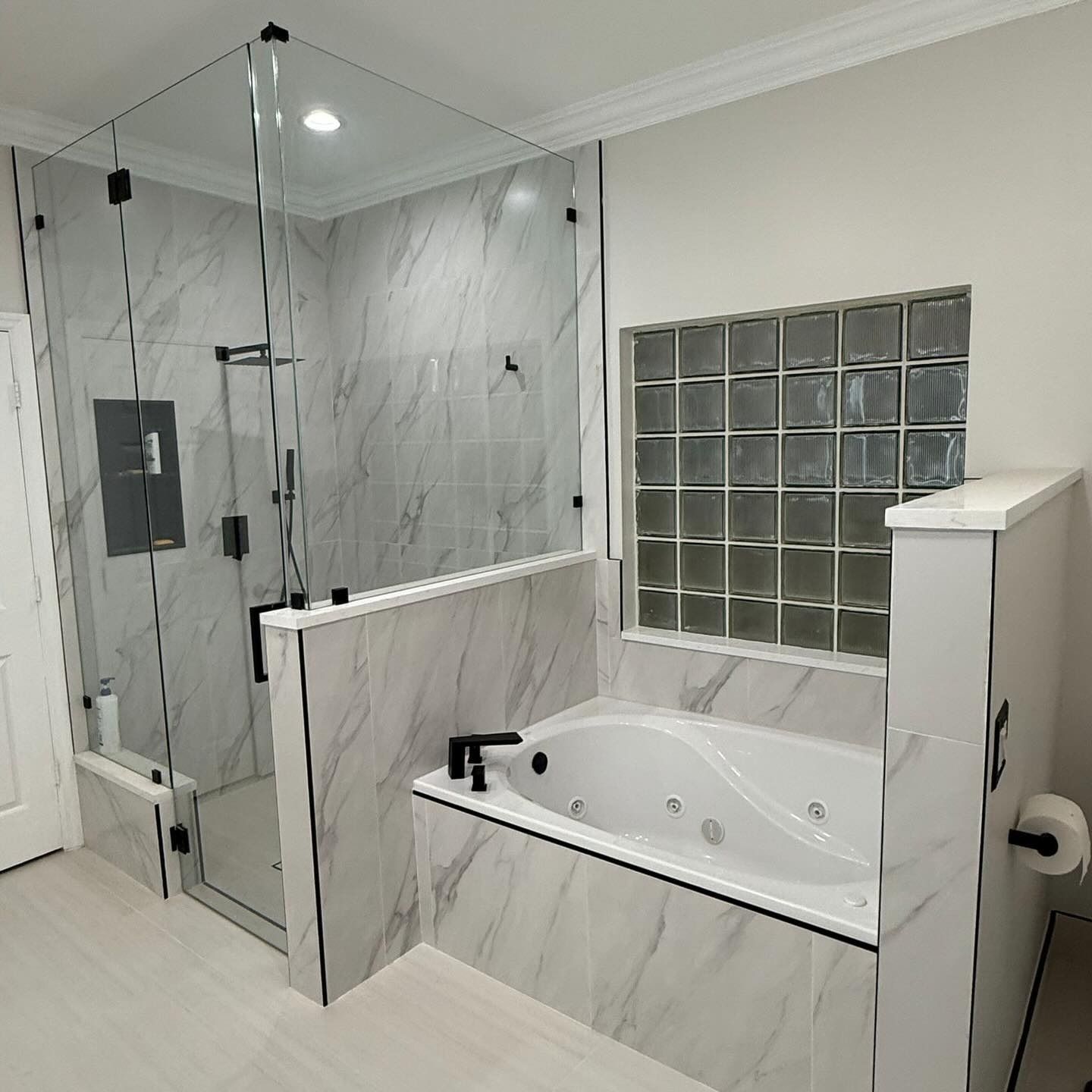 Modern bathroom with glass shower, freestanding tub, marble-style tile, and glass-block window.