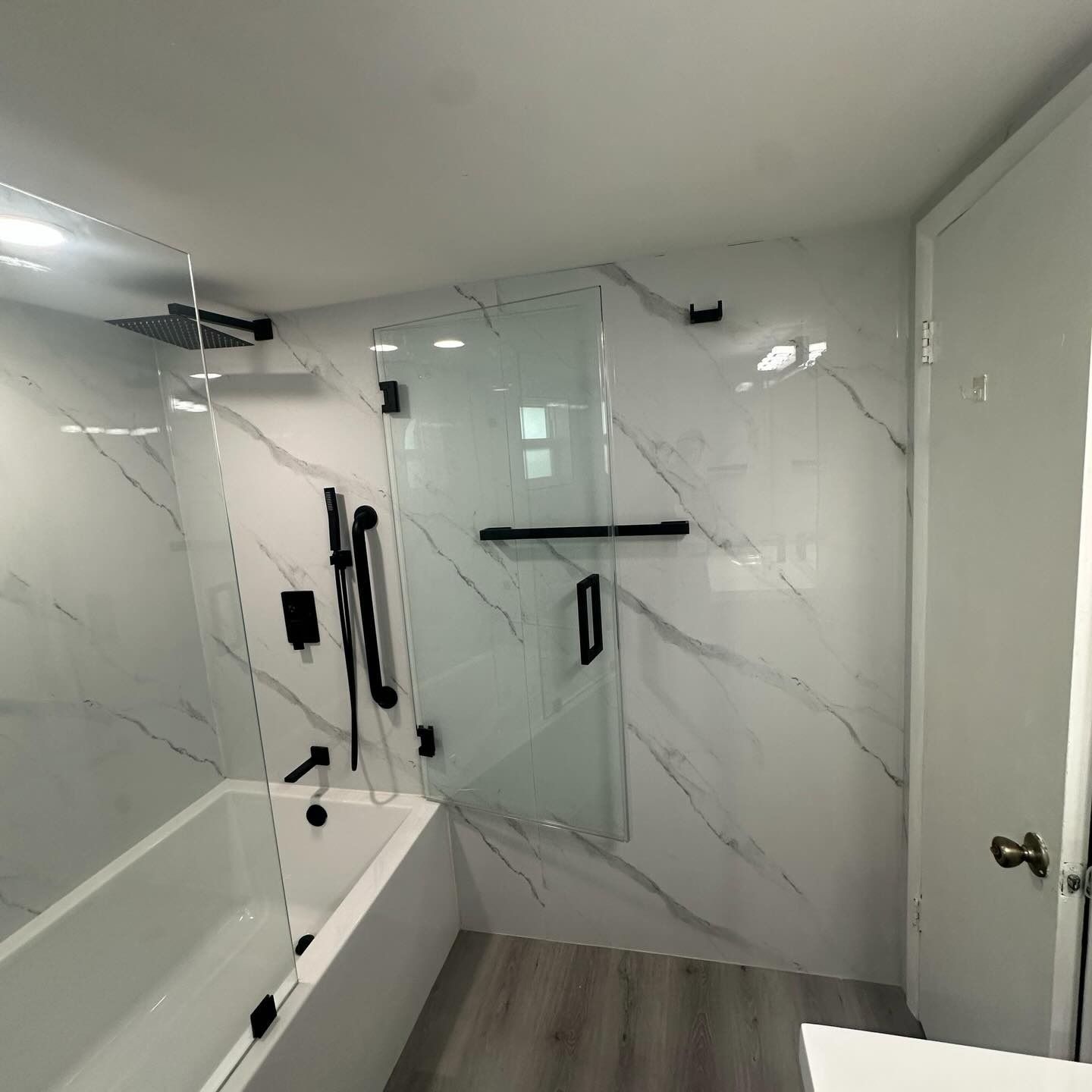 Modern bathroom with glass walk-in shower, white marble walls, and black fixtures
