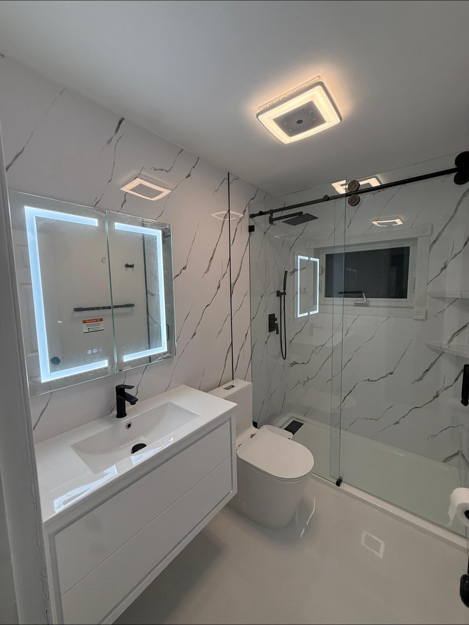 Modern bathroom with illuminated mirror, white vanity, wall-mounted toilet, and glass shower enclosure