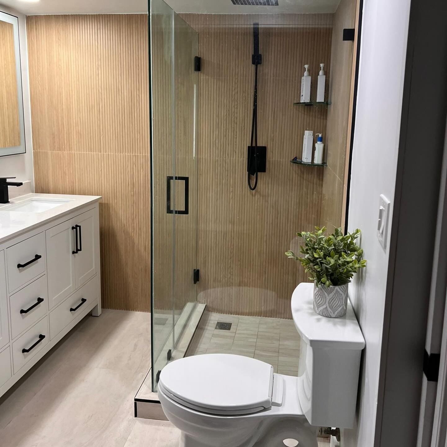 Modern bathroom with glass shower, white toilet, vanity, and wood-textured walls