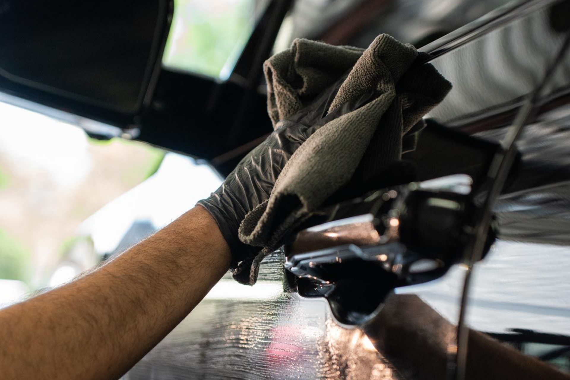 Person in black gloves wiping a black car door with a cloth, likely cleaning it.