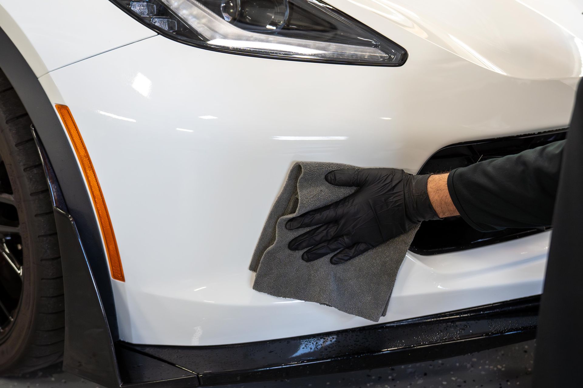 Person in black glove wiping white car bumper with a gray cloth.